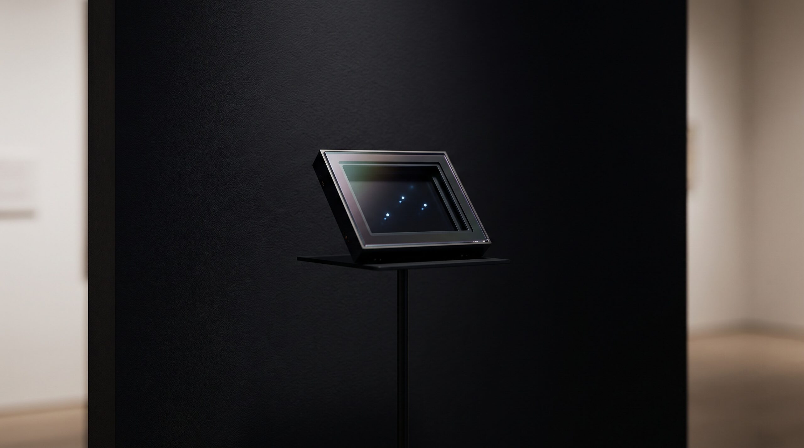 A dark semiconductor CT detector module displayed as a sculptural object on a pedestal against a near-black gallery wall, with a few points of cool light